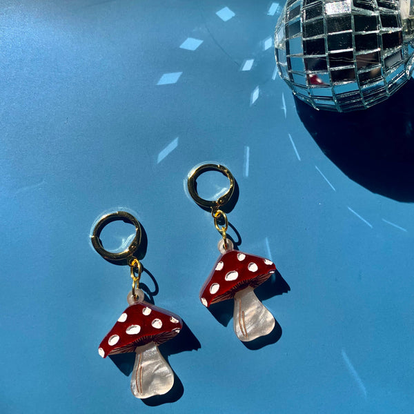 Mushroom-shaped earrings with red caps and white spots on a blue background with disco ball