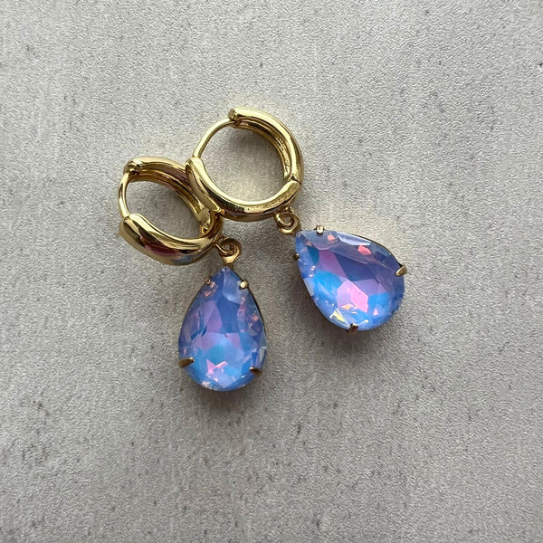 Gold hoop earrings with teardrop-shaped blue gemstones on a gray background