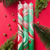 Two swirled red, green, and white candles on a red background with Christmas decorations.