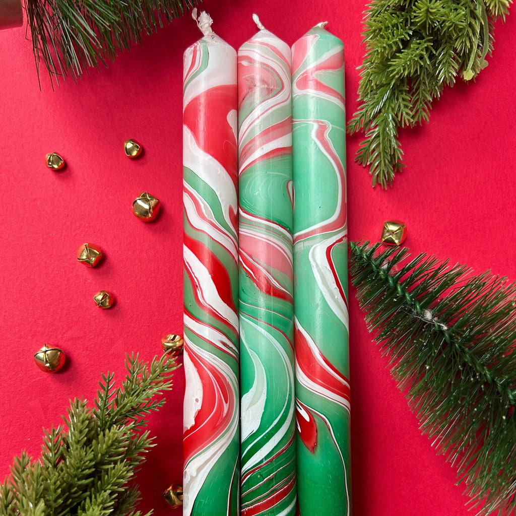 Two swirled red, green, and white candles on a red background with Christmas decorations.
