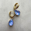 Gold hoop earrings with blue teardrop-shaped gemstones on a gray background