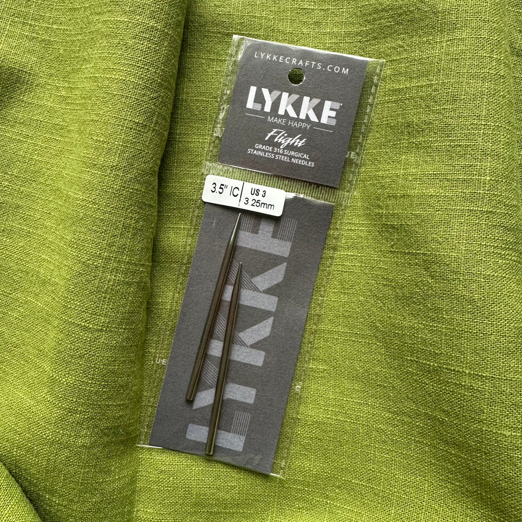 LYKKE knitting needles in packaging on a green fabric background