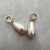Two pearl earrings with gold hooks on a gray surface