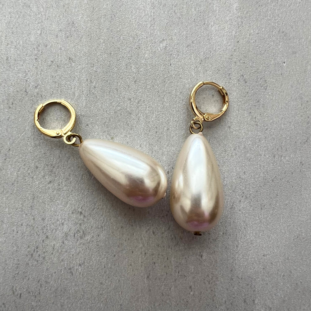 Two pearl earrings with gold hooks on a gray surface