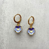 Gold hoop earrings with blue and white flower charms on a light gray background