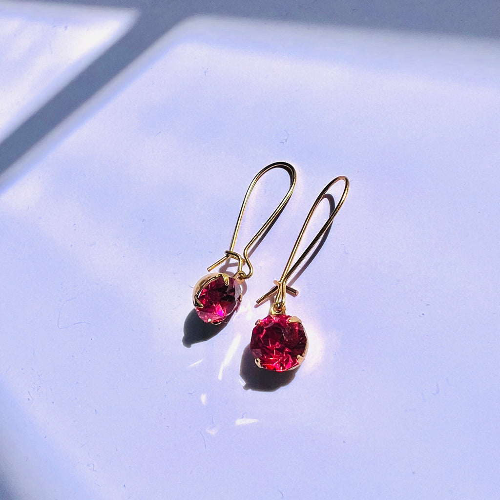 Gold earrings with red gemstones on a light blue background
