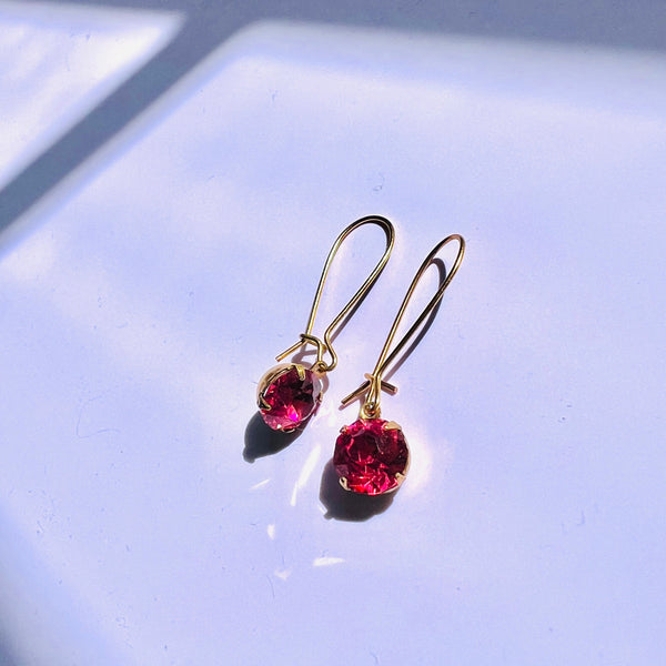 Gold earrings with red gemstones on a light blue background