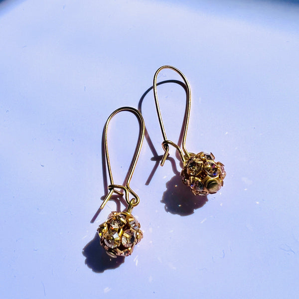 Gold earrings with spherical designs on a light blue background