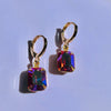 Gold hoop earrings with colorful gemstones on a light purple background