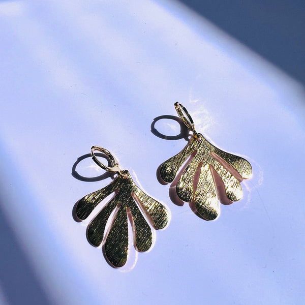 Gold and silver leaf-shaped earrings on a light blue background