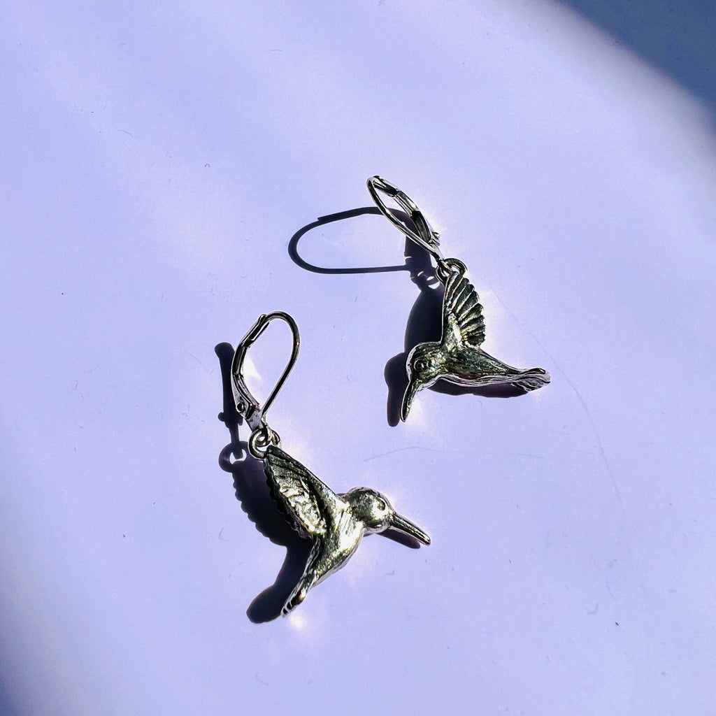 Silver bird-shaped earrings on a light purple background