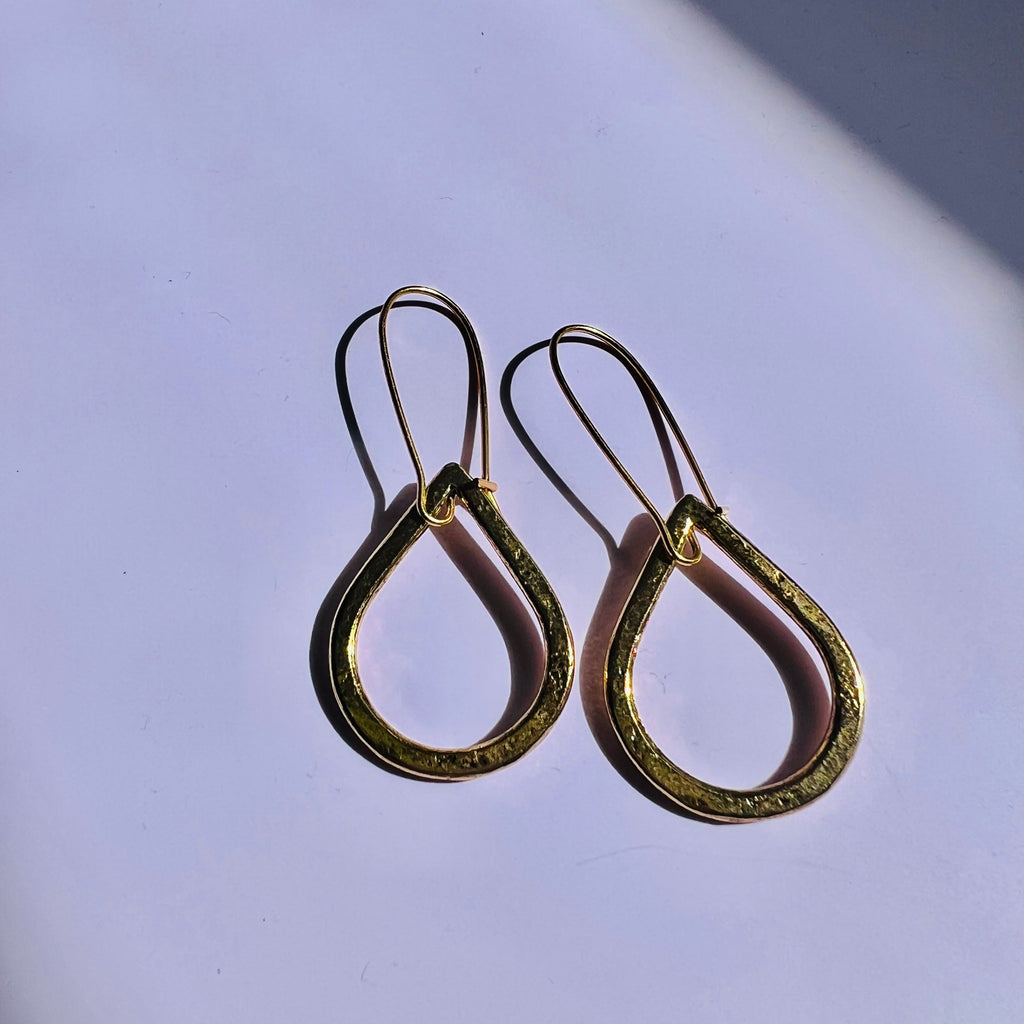 Gold teardrop earrings on a light purple background