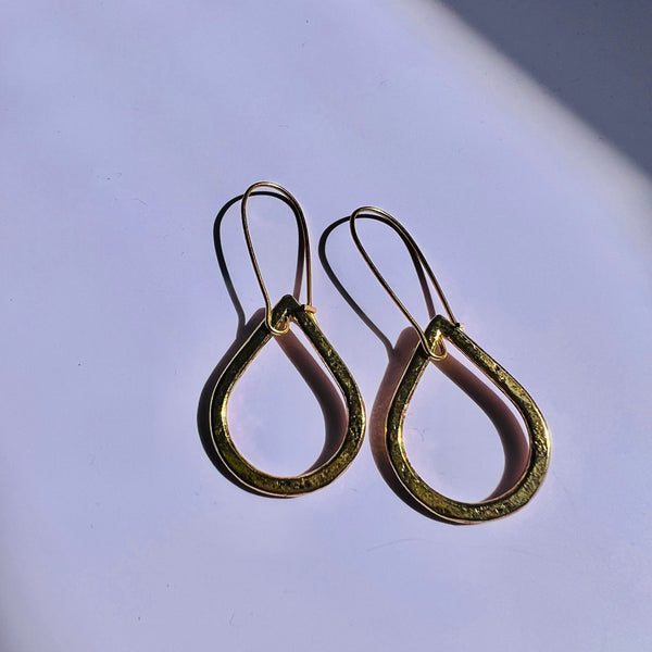 Gold teardrop earrings on a light purple background