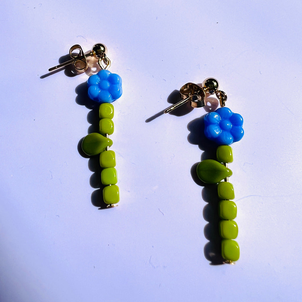 Pair of earrings with blue and green bead designs on a light purple background