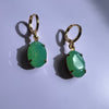 Pair of green earrings with gold hooks on a light purple background