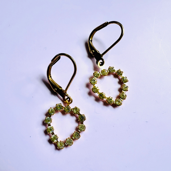 Heart-shaped earrings with green stones on a light purple background