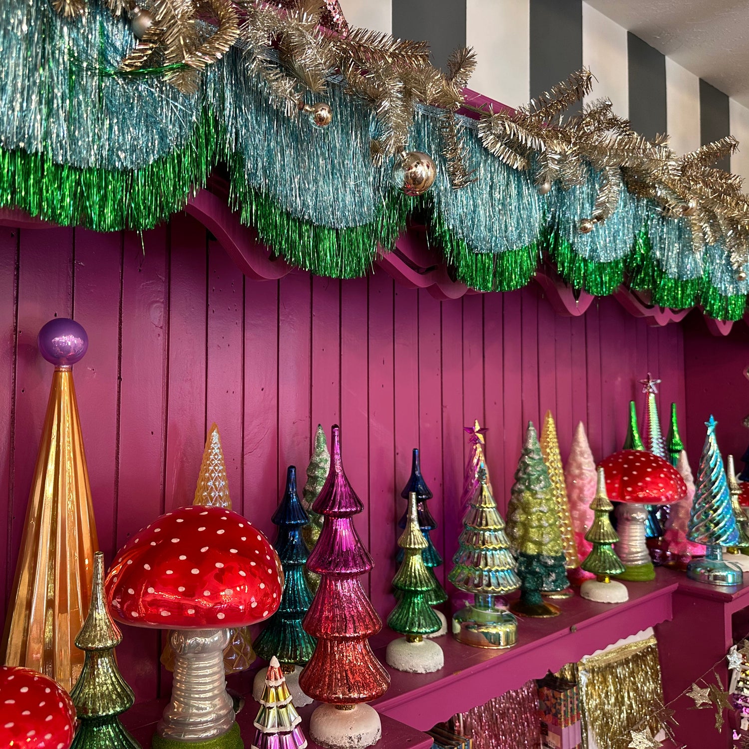 Decorative Christmas trees and garlands on a pink wall with a striped ceiling.