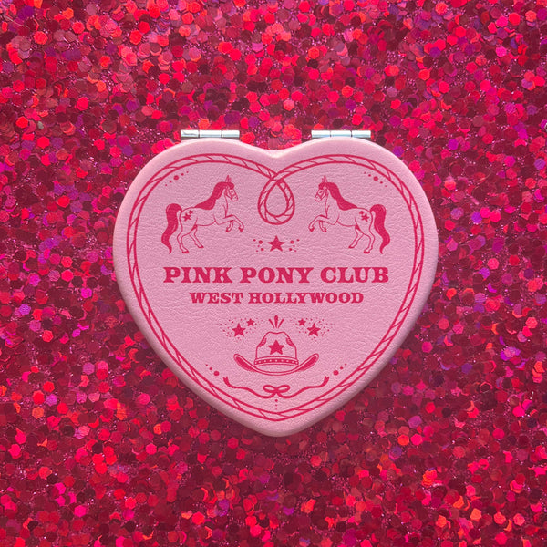 Heart-shaped Pink Pony Club compact mirror on a red glittery background