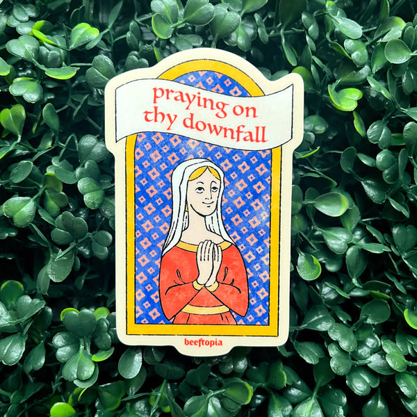 Card with a praying figure and text 'praying on thy downfall' on a green leafy background