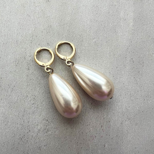 Pearl earrings with gold hooks on a gray surface