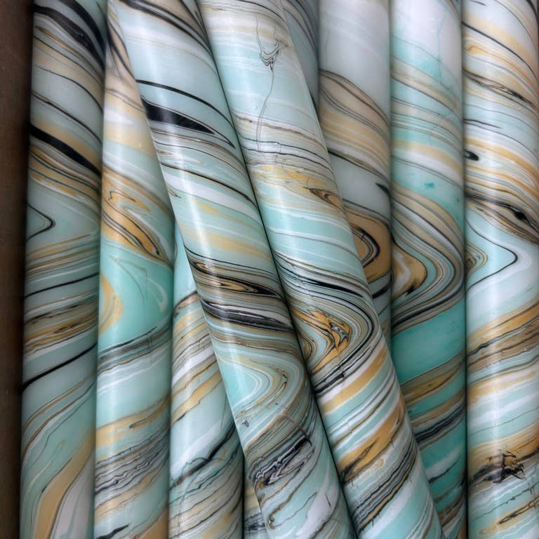 Marble-patterned taper candles in pale aqua, gold and black stacked together