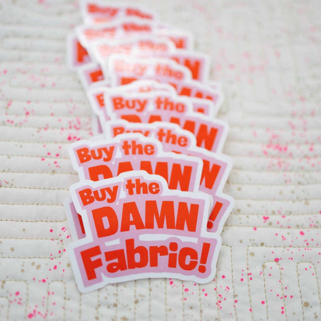 Stack of 'Buy the DAMN Fabric!' stickers on a textured fabric background