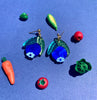 Colorful fruit-shaped earrings on a blue background with small toy fruits and vegetables.