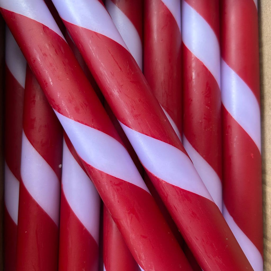 A close-up of several lilac & deep red twisted striped taper candles packed together, filling the frame.