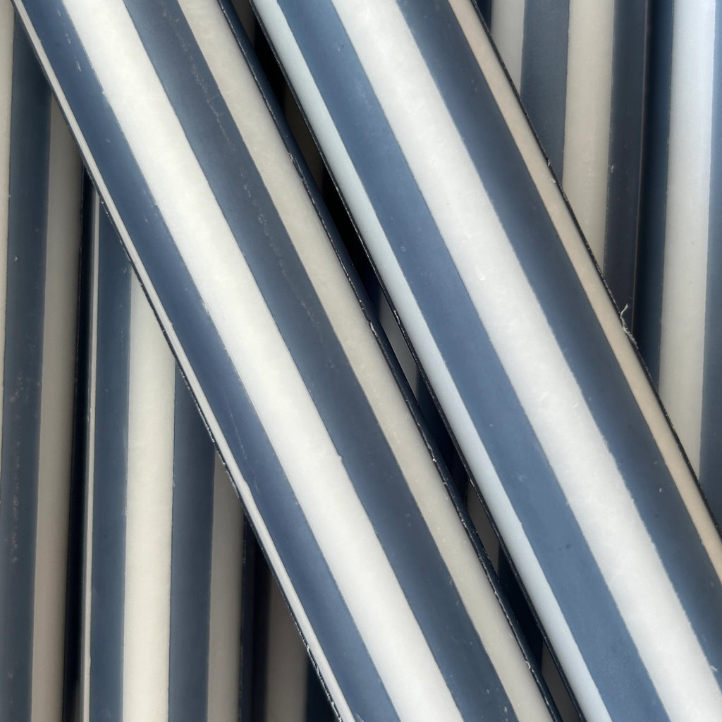 Close-up of striped taper candle with alternating dark navy and off-white vertical bands, filling the frame.