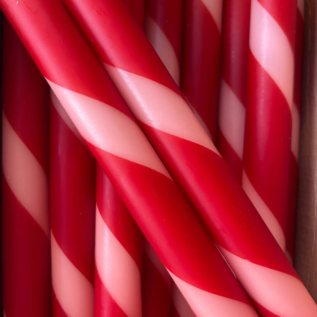 A close-up of red and white striped taper candles arranged tightly together, resembling candy canes.