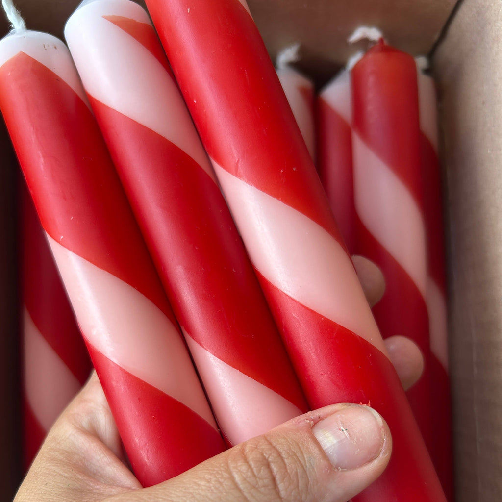 A hand holding a bundle of red and white striped taper candles inside a cardboard box.